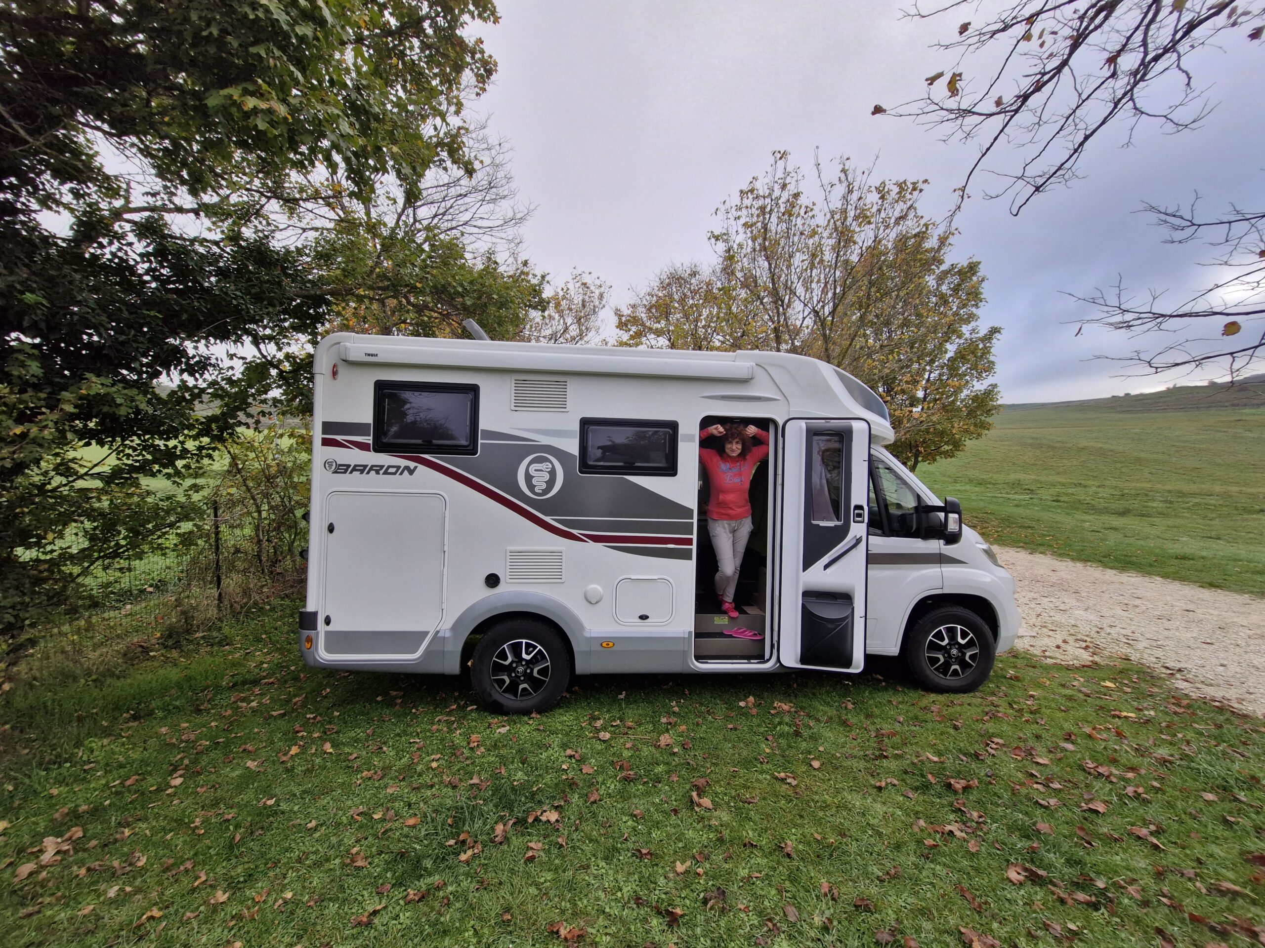 Donna che si affaccia dalla porta di un camper in un parco all'aperto con panorama bellissimo. I migliori consigli di viagi e trekking