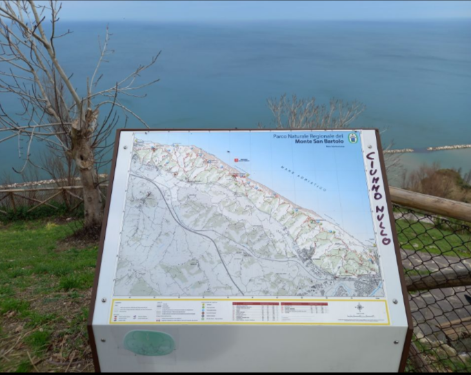 Una cartina aperta che mostra i sentieri del parco di monte san bartolo con dietro un panorama mozzafiato vista mare. I migliori percorsi di trekking