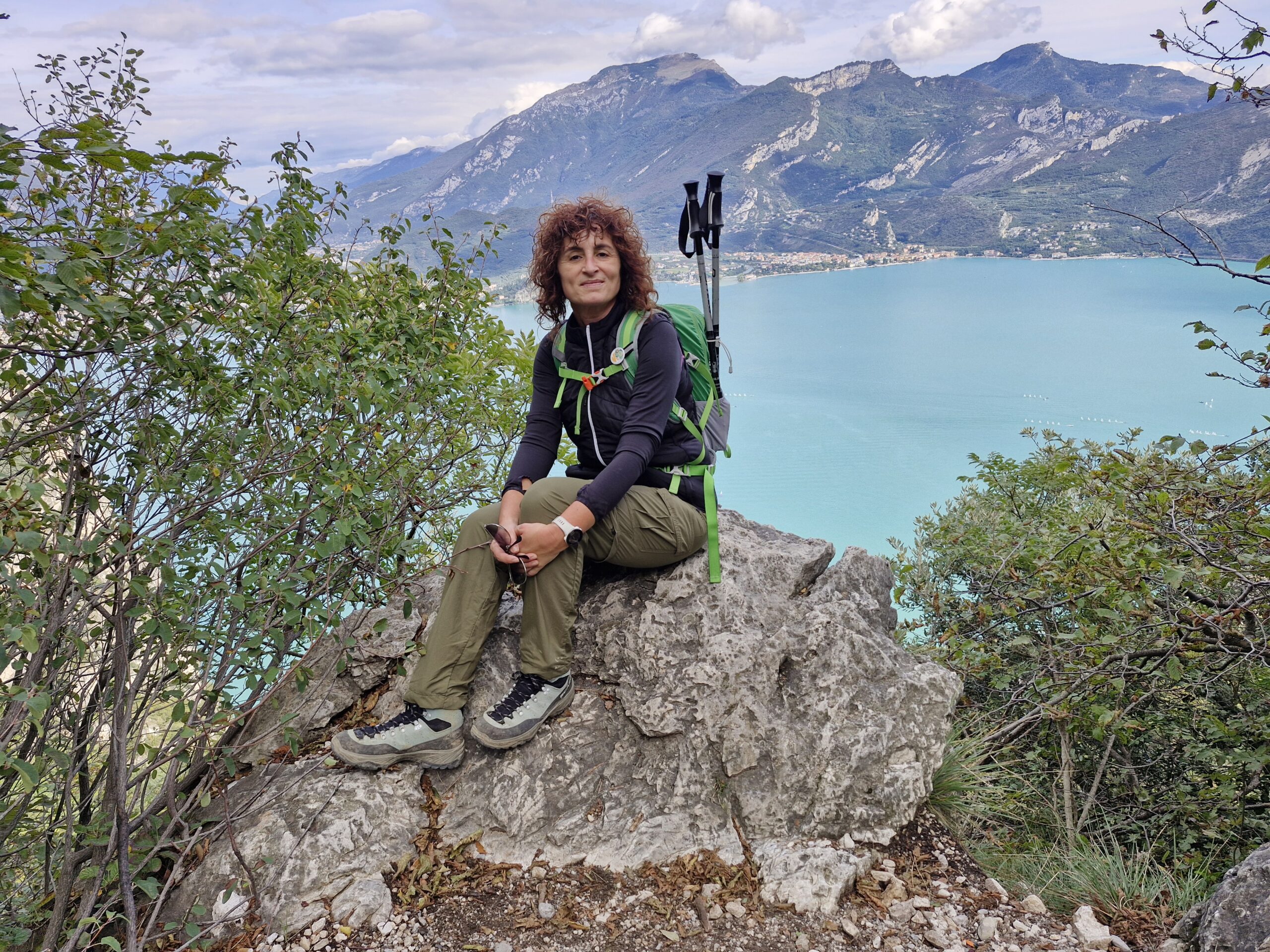 Una donna vestita da trekking con attrezzatura da trekking seduta su una roccia durante un'escursione in montagna vista lago